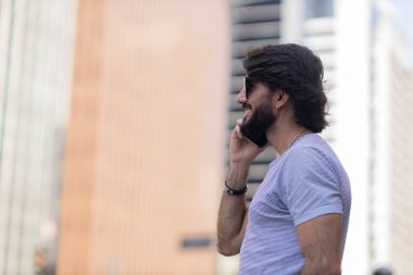 Gündüz vakti akıllı telefon kullanan ve arka planda şehir manzaralı genç bir adamın görüntüsü. Cep telefonu, teknoloji, şehir konsepti. Yüksek kalite fotoğraf