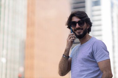 Gündüz vakti akıllı telefon kullanan ve arka planda şehir manzaralı genç bir adamın görüntüsü. Cep telefonu, teknoloji, şehir konsepti. Yüksek kalite fotoğraf