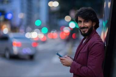 Gece vakti arka planda şehir manzarası olan akıllı telefon kullanan genç bir adamın görüntüsü. Cep telefonu, teknoloji, şehir konsepti. Yüksek kalite fotoğraf