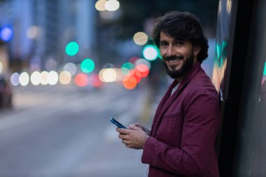Gece vakti arka planda şehir manzarası olan akıllı telefon kullanan genç bir adamın görüntüsü. Cep telefonu, teknoloji, şehir konsepti. Yüksek kalite fotoğraf