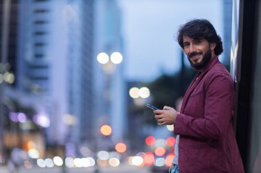 Gece vakti arka planda şehir manzarası olan akıllı telefon kullanan genç bir adamın görüntüsü. Cep telefonu, teknoloji, şehir konsepti. Yüksek kalite fotoğraf