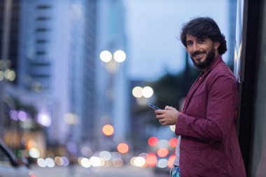 Gece vakti arka planda şehir manzarası olan akıllı telefon kullanan genç bir adamın görüntüsü. Cep telefonu, teknoloji, şehir konsepti. Yüksek kalite fotoğraf