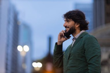 Gece vakti arka planda şehir manzarası olan akıllı telefon kullanan genç bir adamın görüntüsü. Cep telefonu, teknoloji, şehir konsepti. Yüksek kalite fotoğraf