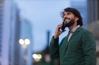 Gece vakti arka planda şehir manzarası olan akıllı telefon kullanan genç bir adamın görüntüsü. Cep telefonu, teknoloji, şehir konsepti. Yüksek kalite fotoğraf
