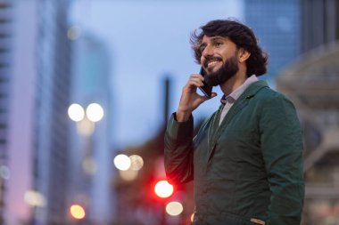 Gece vakti arka planda şehir manzarası olan akıllı telefon kullanan genç bir adamın görüntüsü. Cep telefonu, teknoloji, şehir konsepti. Yüksek kalite fotoğraf