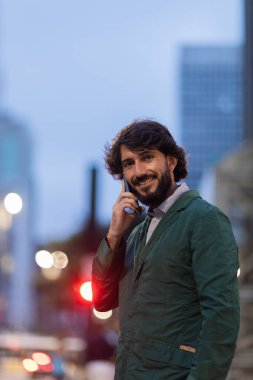 Gece vakti arka planda şehir manzarası olan akıllı telefon kullanan genç bir adamın görüntüsü. Cep telefonu, teknoloji, şehir konsepti. Yüksek kalite fotoğraf