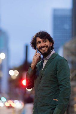 Gece vakti arka planda şehir manzarası olan akıllı telefon kullanan genç bir adamın görüntüsü. Cep telefonu, teknoloji, şehir konsepti. Yüksek kalite fotoğraf