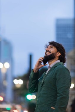 Gece vakti arka planda şehir manzarası olan akıllı telefon kullanan genç bir adamın görüntüsü. Cep telefonu, teknoloji, şehir konsepti. Yüksek kalite fotoğraf