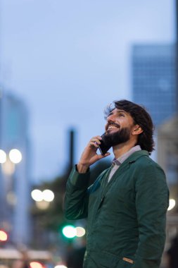 Gece vakti arka planda şehir manzarası olan akıllı telefon kullanan genç bir adamın görüntüsü. Cep telefonu, teknoloji, şehir konsepti. Yüksek kalite fotoğraf