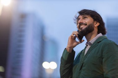 Gece vakti arka planda şehir manzarası olan akıllı telefon kullanan genç bir adamın görüntüsü. Cep telefonu, teknoloji, şehir konsepti. Yüksek kalite fotoğraf
