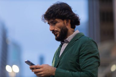 Gece vakti arka planda şehir manzarası olan akıllı telefon kullanan genç bir adamın görüntüsü. Cep telefonu, teknoloji, şehir konsepti. Yüksek kalite fotoğraf