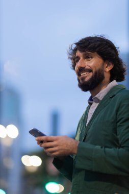 Gece vakti arka planda şehir manzarası olan akıllı telefon kullanan genç bir adamın görüntüsü. Cep telefonu, teknoloji, şehir konsepti. Yüksek kalite fotoğraf