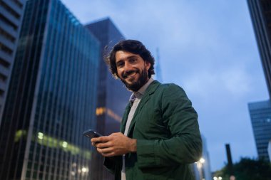 Gece vakti arka planda şehir manzarası olan akıllı telefon kullanan genç bir adamın görüntüsü. Cep telefonu, teknoloji, şehir konsepti. Yüksek kalite fotoğraf