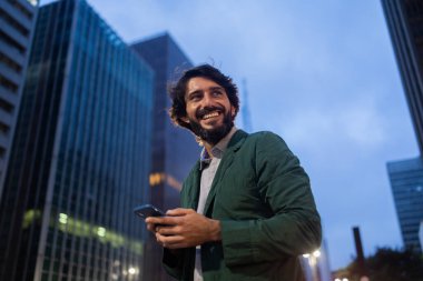 Gece vakti arka planda şehir manzarası olan akıllı telefon kullanan genç bir adamın görüntüsü. Cep telefonu, teknoloji, şehir konsepti. Yüksek kalite fotoğraf