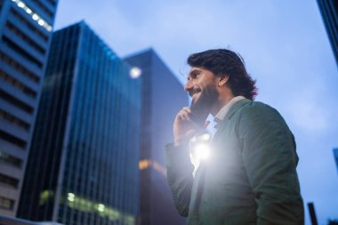 Gece vakti arka planda şehir manzarası olan akıllı telefon kullanan genç bir adamın görüntüsü. Cep telefonu, teknoloji, şehir konsepti. Yüksek kalite fotoğraf