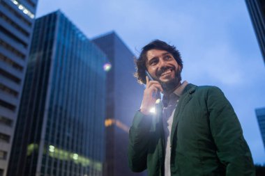 Gece vakti arka planda şehir manzarası olan akıllı telefon kullanan genç bir adamın görüntüsü. Cep telefonu, teknoloji, şehir konsepti. Yüksek kalite fotoğraf