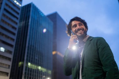 Gece vakti arka planda şehir manzarası olan akıllı telefon kullanan genç bir adamın görüntüsü. Cep telefonu, teknoloji, şehir konsepti. Yüksek kalite fotoğraf