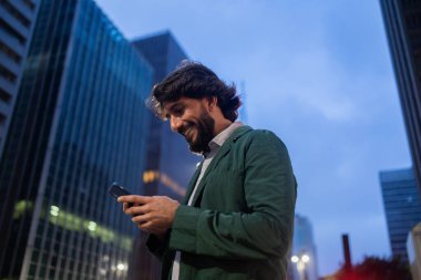 Gece vakti arka planda şehir manzarası olan akıllı telefon kullanan genç bir adamın görüntüsü. Cep telefonu, teknoloji, şehir konsepti. Yüksek kalite fotoğraf