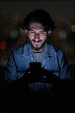 Arka planda şehir manzarası olan gece akıllı telefon kullanan genç bir adamın ön görüntüsü. Cep telefonu, teknoloji, konsept. Yüksek kalite fotoğraf