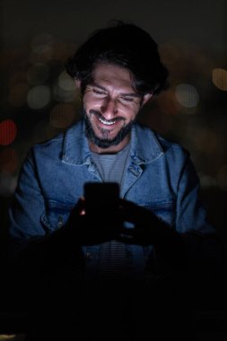 Arka planda şehir manzarası olan gece akıllı telefon kullanan genç bir adamın ön görüntüsü. Cep telefonu, teknoloji, konsept. Yüksek kalite fotoğraf