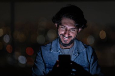 Arka planda şehir manzarası olan gece akıllı telefon kullanan genç bir adamın ön görüntüsü. Cep telefonu, teknoloji, konsept. Yüksek kalite fotoğraf