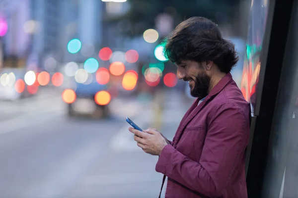 Gece vakti arka planda şehir manzarası olan akıllı telefon kullanan genç bir adamın görüntüsü. Cep telefonu, teknoloji, şehir konsepti. Yüksek kalite fotoğraf