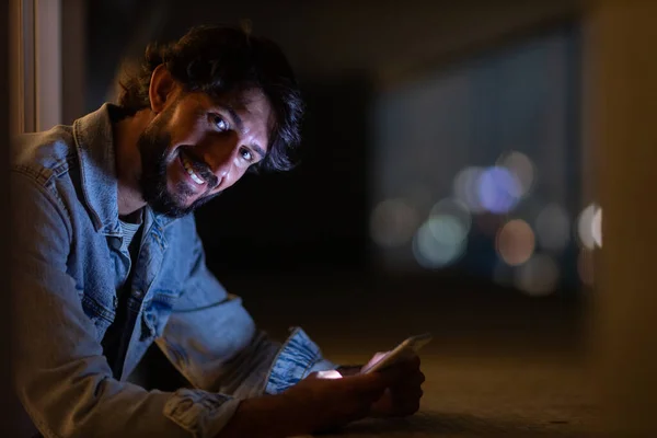 背景に都市の風景とのバルコニーで夜の時間にスマートフォンを使用して若い男のサイドビュー 携帯電話技術コンセプト 高品質の写真 — ストック写真