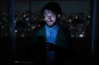 Arka planda şehir manzarası olan gece akıllı telefon kullanan genç bir adamın ön görüntüsü. Cep telefonu, teknoloji, konsept. Yüksek kalite fotoğraf