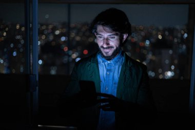 Arka planda şehir manzarası olan gece akıllı telefon kullanan genç bir adamın ön görüntüsü. Cep telefonu, teknoloji, konsept. Yüksek kalite fotoğraf