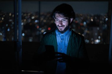Arka planda şehir manzarası olan gece akıllı telefon kullanan genç bir adamın ön görüntüsü. Cep telefonu, teknoloji, konsept. Yüksek kalite fotoğraf
