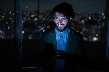 Arka planda şehir manzarası olan gece akıllı telefon kullanan genç bir adamın ön görüntüsü. Cep telefonu, teknoloji, konsept. Yüksek kalite fotoğraf