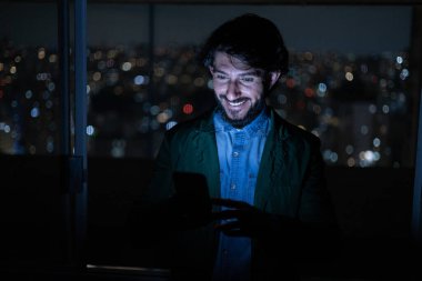 Arka planda şehir manzarası olan gece akıllı telefon kullanan genç bir adamın ön görüntüsü. Cep telefonu, teknoloji, konsept. Yüksek kalite fotoğraf