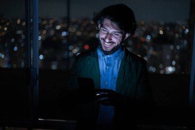 Arka planda şehir manzarası olan gece akıllı telefon kullanan genç bir adamın ön görüntüsü. Cep telefonu, teknoloji, konsept. Yüksek kalite fotoğraf