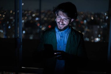 Arka planda şehir manzarası olan gece akıllı telefon kullanan genç bir adamın ön görüntüsü. Cep telefonu, teknoloji, konsept. Yüksek kalite fotoğraf