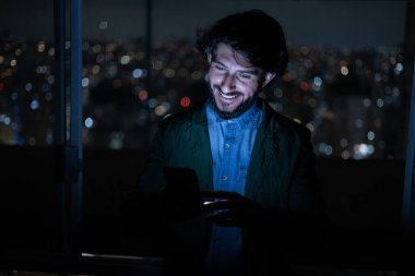 Arka planda şehir manzarası olan gece akıllı telefon kullanan genç bir adamın ön görüntüsü. Cep telefonu, teknoloji, konsept. Yüksek kalite fotoğraf
