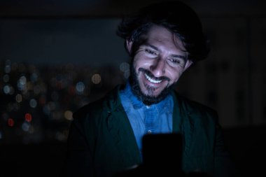 Arka planda şehir manzarası olan gece akıllı telefon kullanan genç bir adamın ön görüntüsü. Cep telefonu, teknoloji, konsept. Yüksek kalite fotoğraf