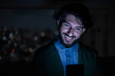 Arka planda şehir manzarası olan gece akıllı telefon kullanan genç bir adamın ön görüntüsü. Cep telefonu, teknoloji, konsept. Yüksek kalite fotoğraf