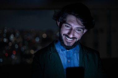 Arka planda şehir manzarası olan gece akıllı telefon kullanan genç bir adamın ön görüntüsü. Cep telefonu, teknoloji, konsept. Yüksek kalite fotoğraf