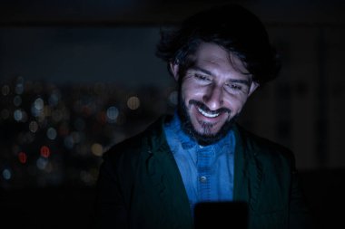 Arka planda şehir manzarası olan gece akıllı telefon kullanan genç bir adamın ön görüntüsü. Cep telefonu, teknoloji, konsept. Yüksek kalite fotoğraf