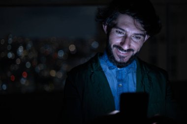 Arka planda şehir manzarası olan gece akıllı telefon kullanan genç bir adamın ön görüntüsü. Cep telefonu, teknoloji, konsept. Yüksek kalite fotoğraf