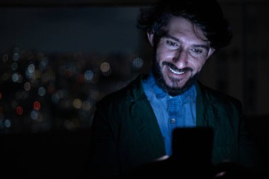 Arka planda şehir manzarası olan gece akıllı telefon kullanan genç bir adamın ön görüntüsü. Cep telefonu, teknoloji, konsept. Yüksek kalite fotoğraf
