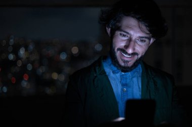 Arka planda şehir manzarası olan gece akıllı telefon kullanan genç bir adamın ön görüntüsü. Cep telefonu, teknoloji, konsept. Yüksek kalite fotoğraf