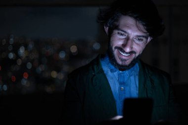 Arka planda şehir manzarası olan gece akıllı telefon kullanan genç bir adamın ön görüntüsü. Cep telefonu, teknoloji, konsept. Yüksek kalite fotoğraf