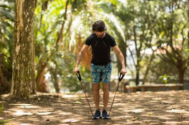 Parkta lastik bantlarla çalışan güçlü bir adam. Spor yaparken spor malzemeleriyle spor yapan erkek sporcu. Yüksek kalite fotoğraf. İyi, sağlıklı, sağlık, egzersiz konsepti. 
