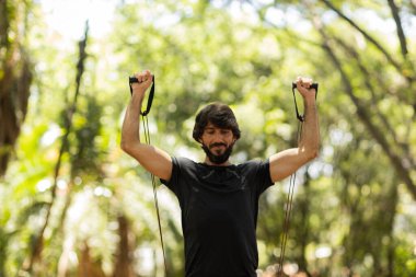 Parkta lastik bantlarla çalışan güçlü bir adam. Spor yaparken spor malzemeleriyle spor yapan erkek sporcu. Yüksek kalite fotoğraf. İyi, sağlıklı, sağlık, egzersiz konsepti. 