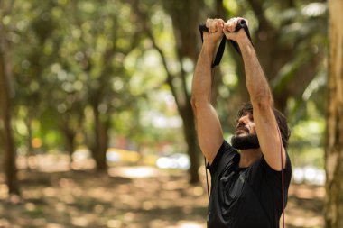 Parkta lastik bantlarla çalışan güçlü bir adam. Spor yaparken spor malzemeleriyle spor yapan erkek sporcu. Yüksek kalite fotoğraf. İyi, sağlıklı, sağlık, egzersiz konsepti. 