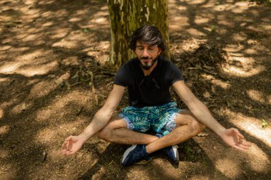 Genç adam meditasyon yapıyor. Güneşli havada yoga ve meditasyon pratiği. Parkta bir gün. Yüksek kalite fotoğraf. İyi, sağlıklı, ruhani bir konsept. 