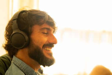 Oturma odasında kulağında kulaklıkla müzik dinleyen genç bir adamın görüntüsü. Yüksek kalite fotoğraf. Cep telefonu, teknoloji, müzik, kentsel yaşam, iyi hisset.