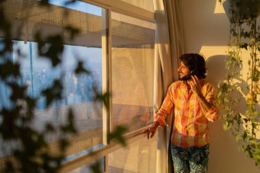 Kulağında kulaklıklarla müzik dinleyen genç bir adamın yan görüntüsü. Arka planda şehir manzarası var. Yüksek kalite fotoğraf. Cep telefonu, teknoloji, müzik, kentsel yaşam, iyi hisset.