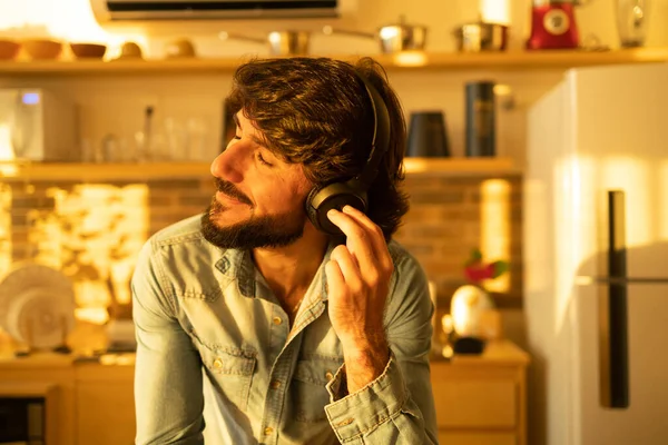Evinin mutfağında kulağında kulaklıkla müzik dinleyen genç bir adamın görüntüsü. Yüksek kalite fotoğraf. Cep telefonu, teknoloji, müzik, kentsel yaşam, iyi hisset.